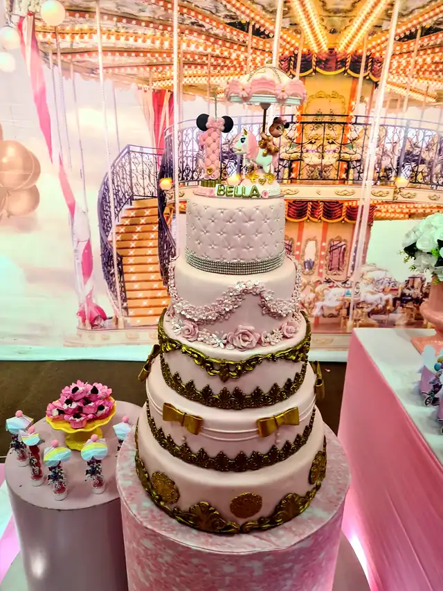 Bolo de festa de quatro andares, em rosa e dourado, com doces decorados ao lado