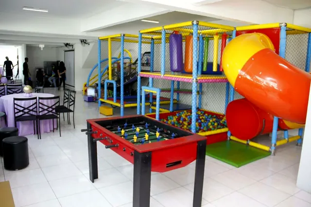 Pebolim vermelho à frente da estrutura de brinquedos com escorregador laranja