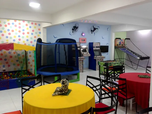 Mesas coloridas, cama elástica e área de jogos ao fundo do salão