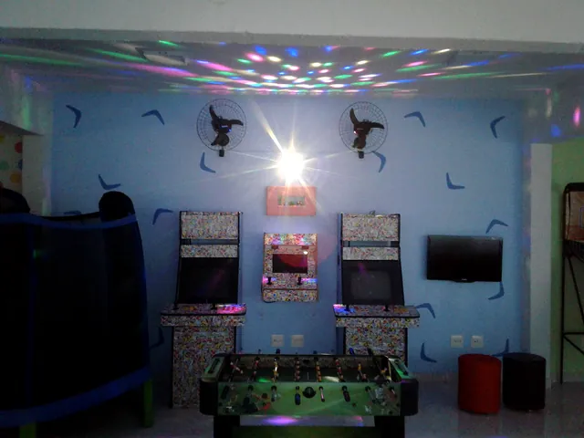 Sala de jogos com fliperamas, pebolim e luzes coloridas no teto