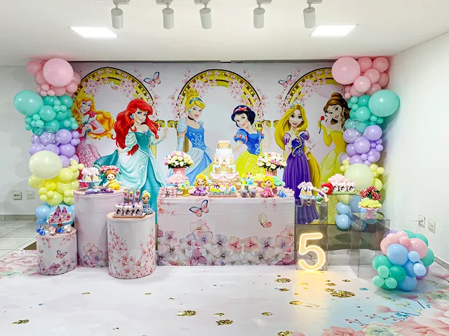 Mesa de festa com tema de princesas, painel em arcos e balões em tons de verde-água e rosa