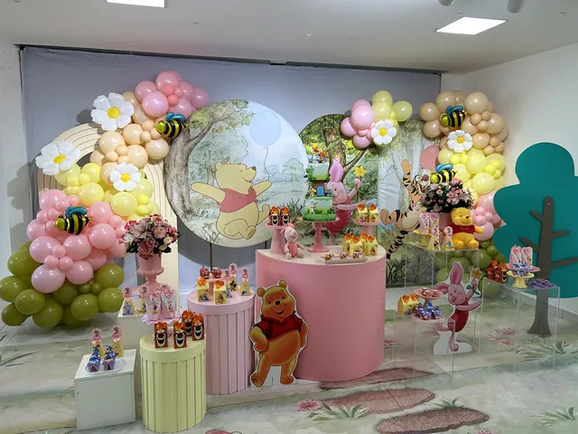 Festa com tema do Ursinho Pooh, balões em amarelo, rosa e verde, e mesas redondas