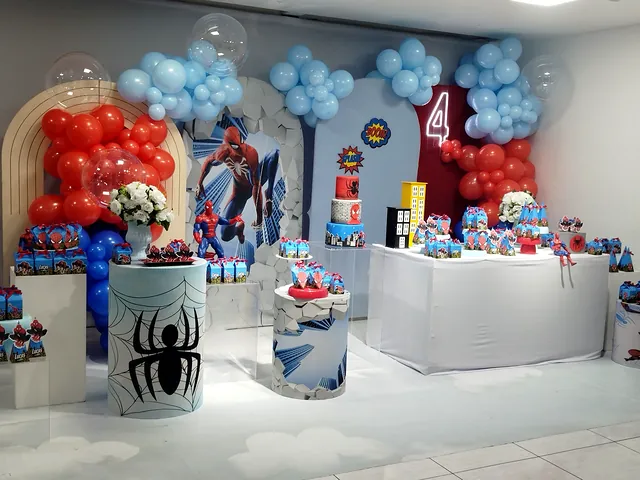 Festa com tema de super-heróis, balões vermelhos e azuis e mesas brancas