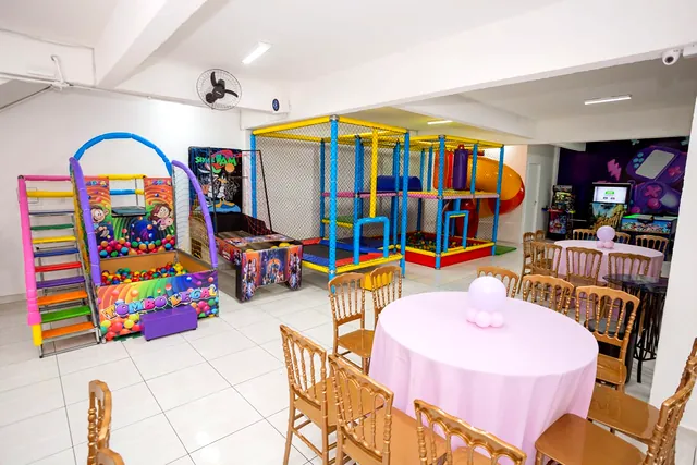 Salão do Boomerang visto por inteiro: mesas redondas com cadeiras de madeira e, ao fundo, a estrutura de brinquedos colorida